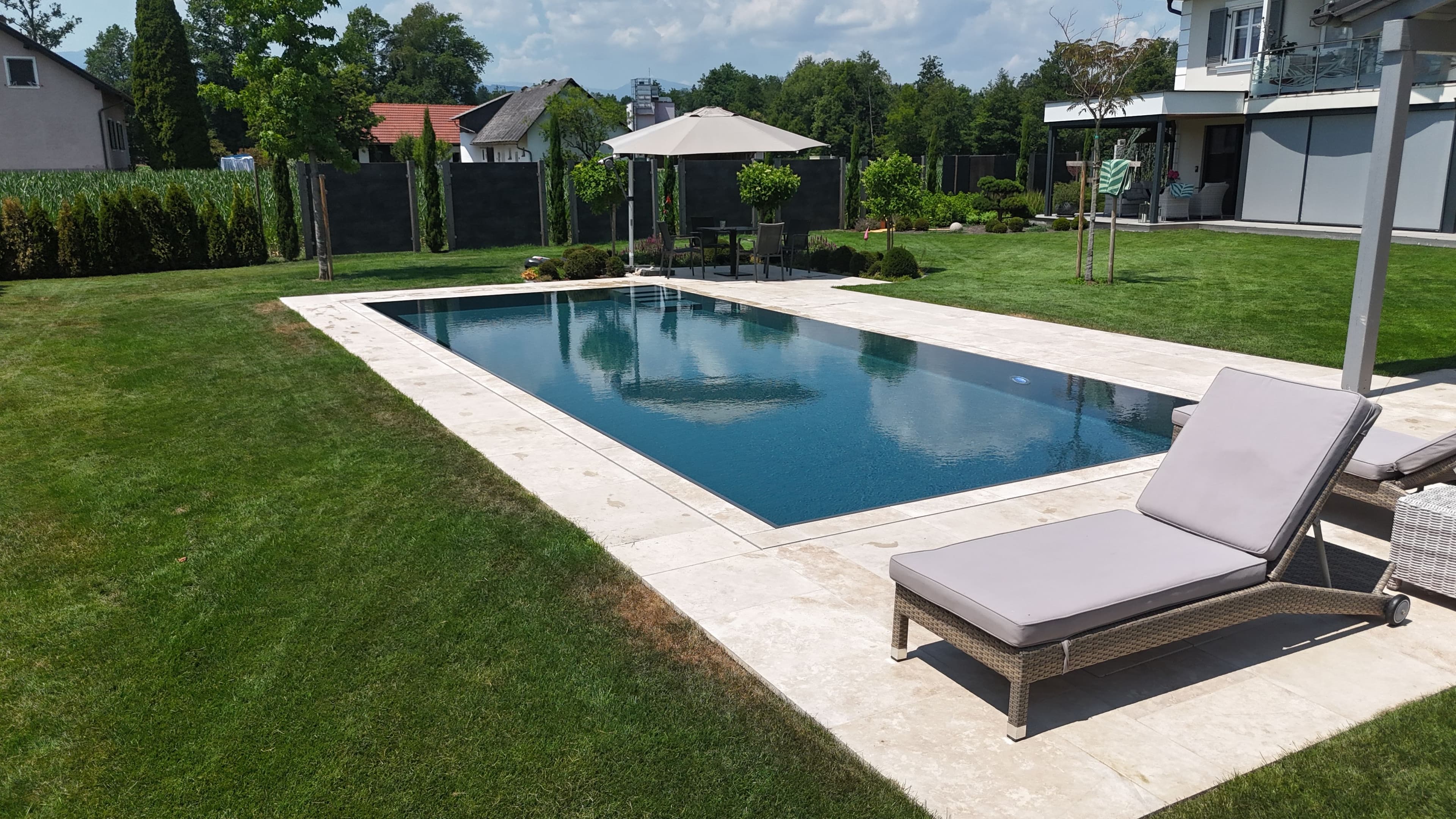 Massivpool mit AquaLite-Überlaufrinne und Holzdeck, eingebettet in die Landschaft