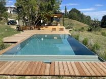 Massivpool mit AquaLite-Überlaufrinne und Holzdeck, eingebettet in die Landschaft